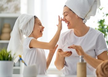 mother and daoughter in the bathroom, laughing as daughter puts cream on mother's nose