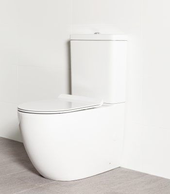 Milu Odourless Crest back-to-wall toilet angled side view with toilet seat down. Positioned against white tiled wall on warm grey coloured floor tiles