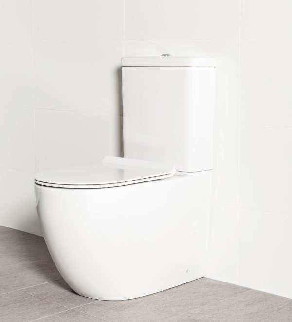 Milu Odourless Crest back-to-wall toilet angled side view with toilet seat down. Positioned against white tiled wall on warm grey coloured floor tiles