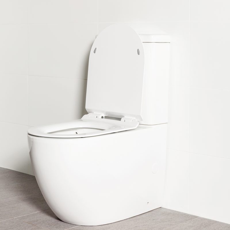Milu Odourless Crest back-to-wall toilet angled side view with toilet seat up. Positioned against white tiled wall on warm grey coloured floor tiles