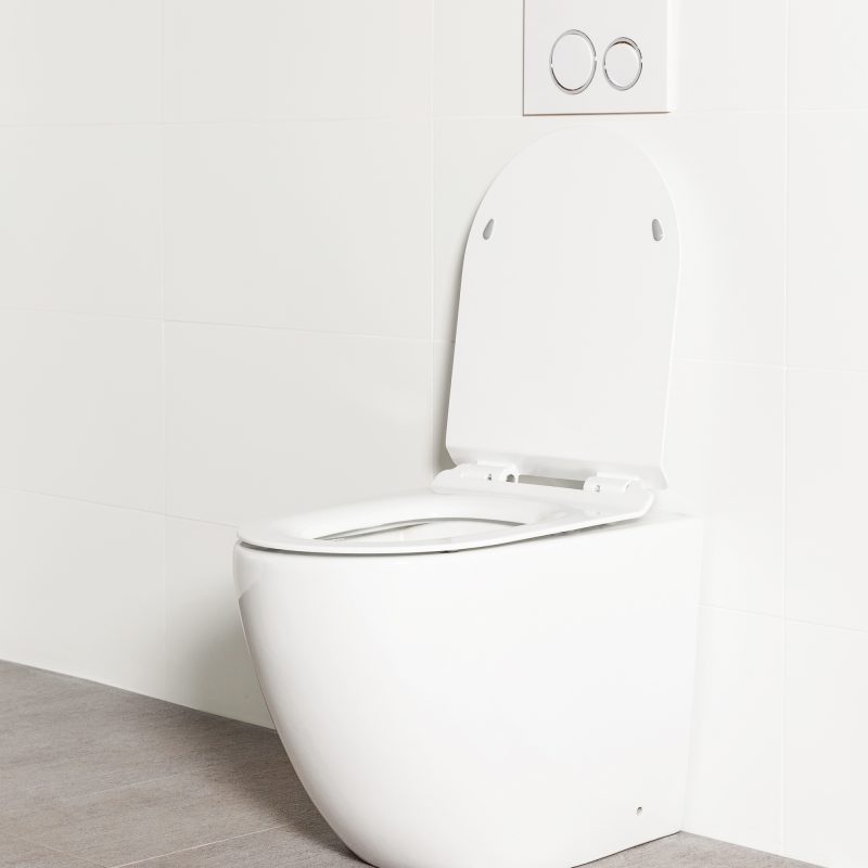 Milu Odourless Crest in-wall floor mounted toilet angled side view with toilet seat up and white flush plate. Toilet has curved pan and minimal design